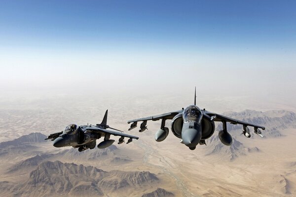 A pair of fighter jets flying in the sky over the mountains