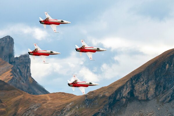 Four fighter jets are flying over the mountains