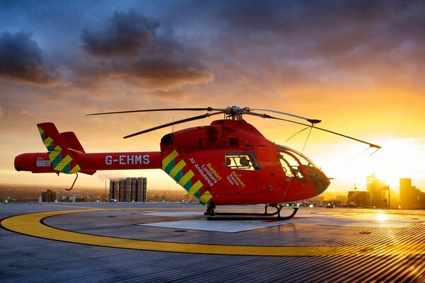 Czerwony helikopter stoi na platformie o zachodzie słońca
