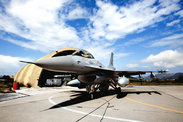 A fighter jet near a hangar with a blue sky