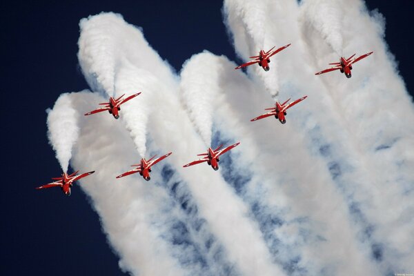 White tails of smoke behind red planes at an air show