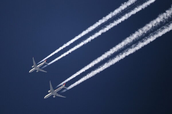 Two planes flying in the sky and leaving a trail