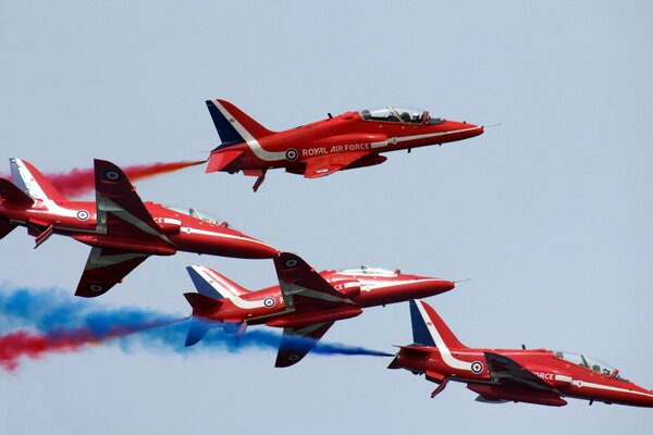 Against the background of a clear sky, red planes emit multicolored smoke