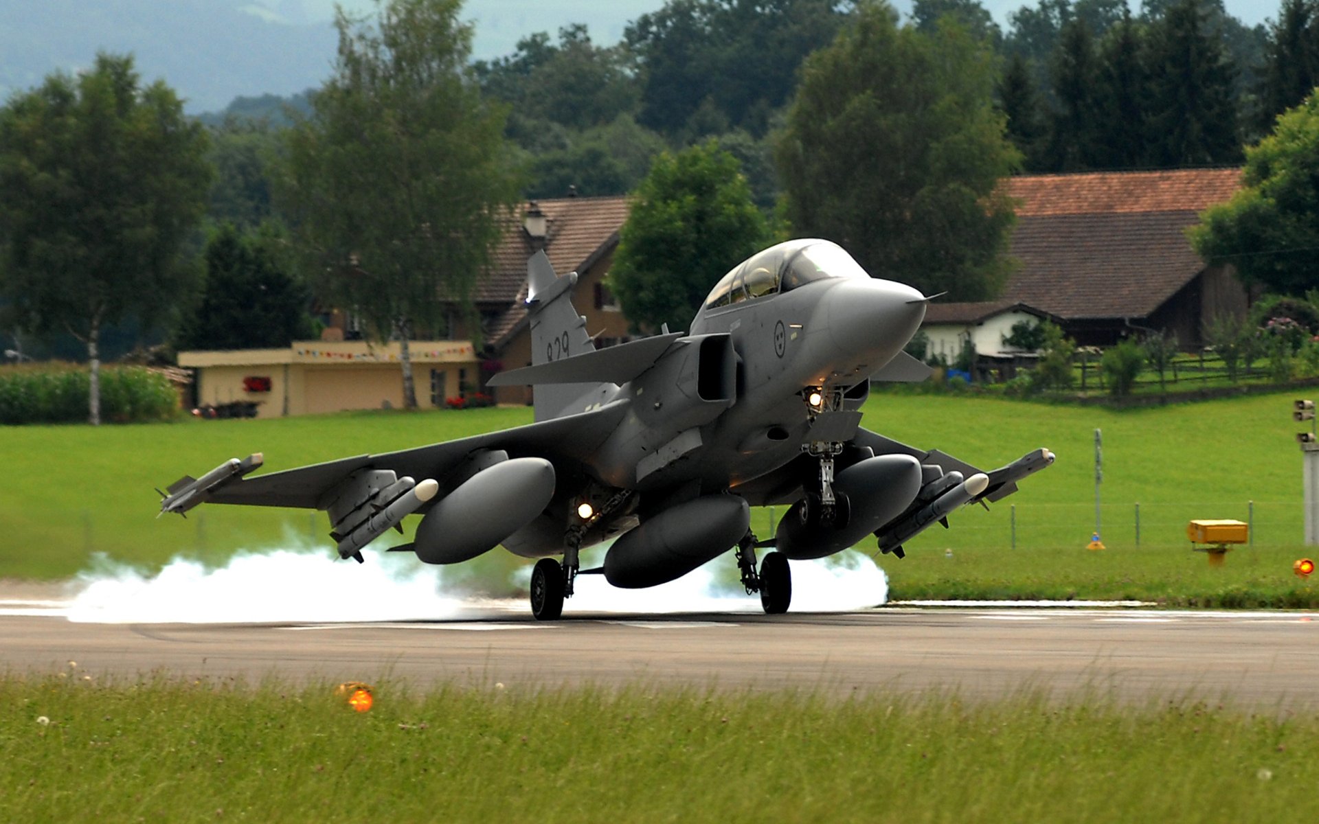 avión saab jas 39 gripen sueco multiusos caza cuarta generación despegue foto aeródromo raya hierba árboles casas