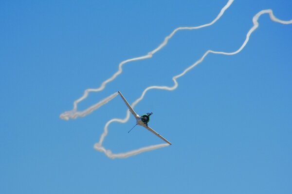 A plane in a blue sky with a tail of smoke