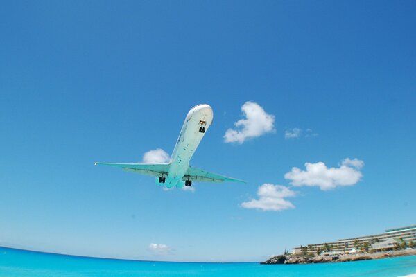 The plane flies over the clear ocean and over hotels