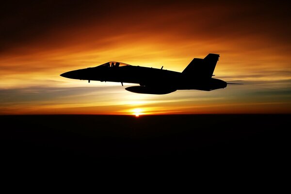 A dark plane is flying against the background of a beautiful sunset