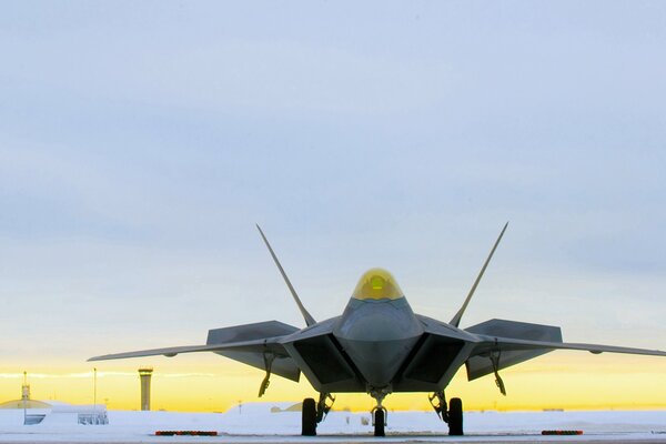 El caza Raptor se encuentra en el aeródromo en el contexto de la puesta del sol