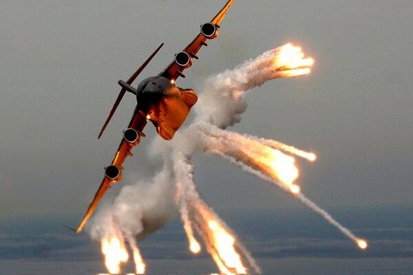 A huge plane flying in the sky releases fire and smoke