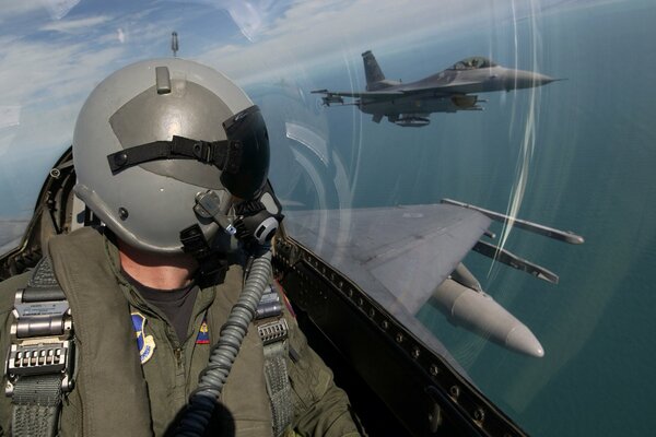 A military pilot watches a plane flying nearby from the cockpit