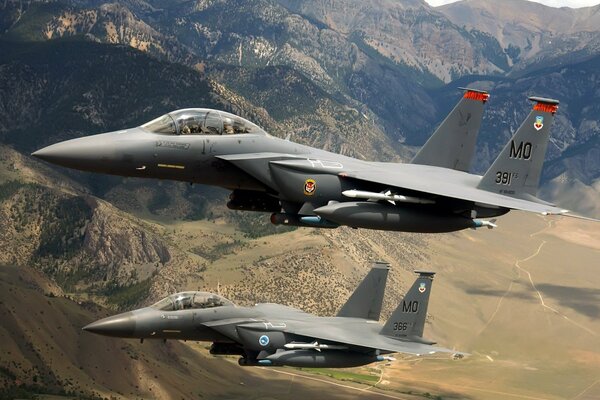 Two fighter planes are flying among the mountains