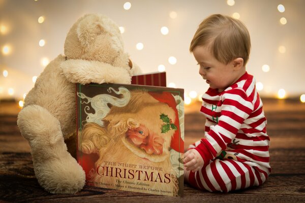 Ребенок в полосатлй пижаме читает книжку и сидит с игрушкой