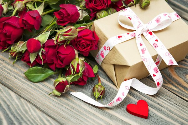 A gift box and red roses are hanging on a wooden table