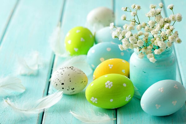 Easter eggs on a blue wooden table, a blue vase with flowers and feathers