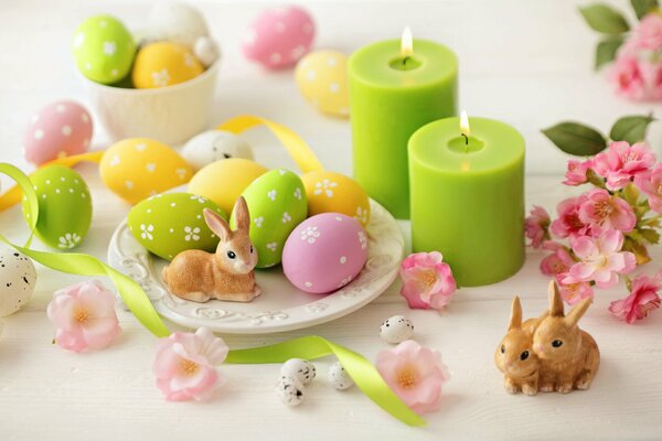 Conejito de Pascua en un plato de huevos pintados. Velas verdes. Pascua