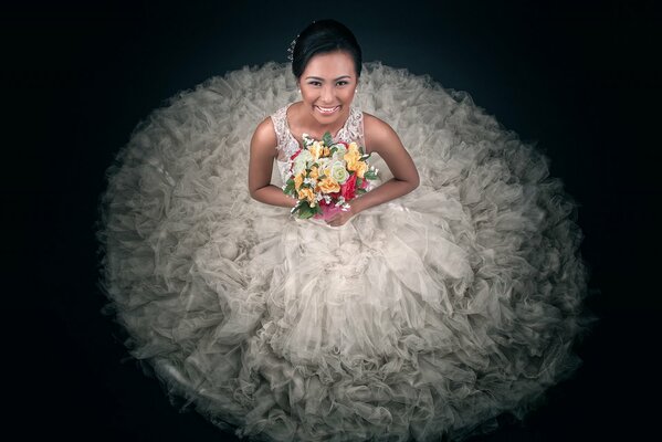 Braut in einem üppigen Kleid mit einem Blumenstrauß auf schwarzem Hintergrund