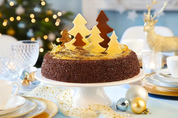 Christmas homemade cake with sweet scraps on the background of a shining Christmas beauty a Christmas tree a deer Christmas balls and beautiful white dishes