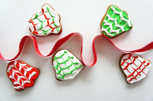 Bright colored gingerbread cookies in the shape of bells are beautifully presented next to a red wavy ribbon