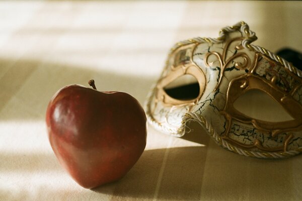 Karnevalsmaske und ein großer roter Apfel im Schatten des Raumes