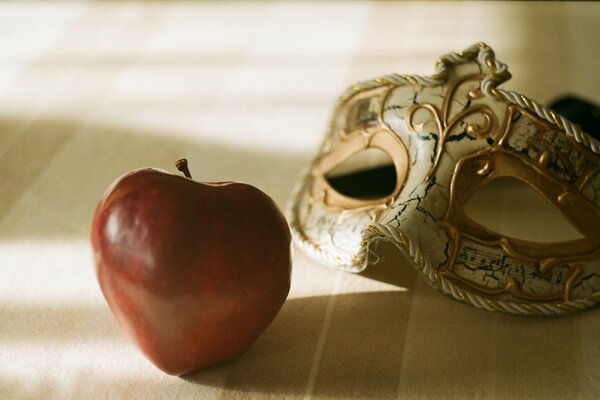 Carnival mask and a big red apple in the shadow of the room