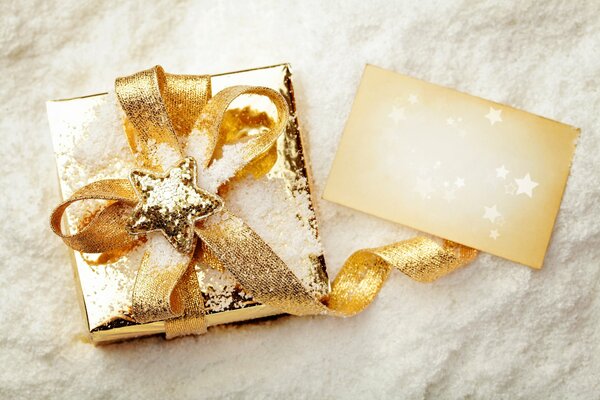 Regalo de año nuevo con cinta dorada y estrella en el fondo de la nieve