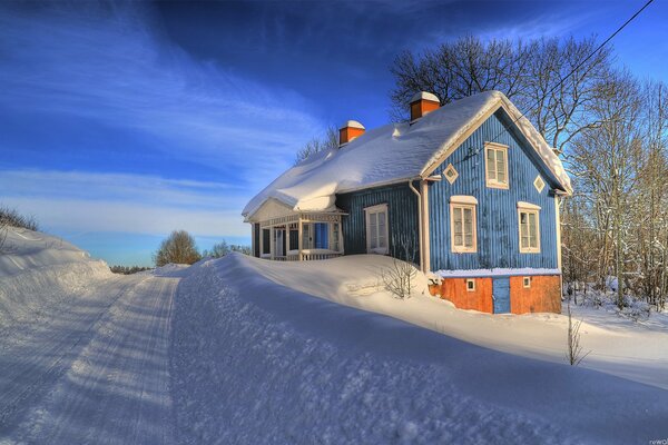 Casa de campo azul en invierno. Nieve en el techo