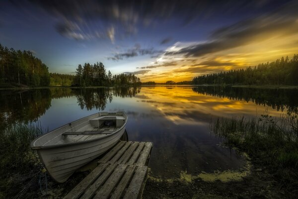 Зеркальное отражение красок заката на озере. Лодка у мостика