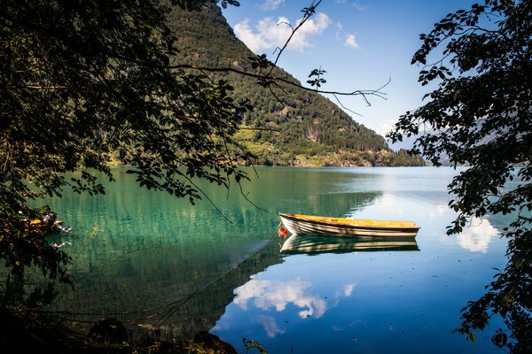 Entre los árboles se ve una alta montaña y un lago en el que el barco