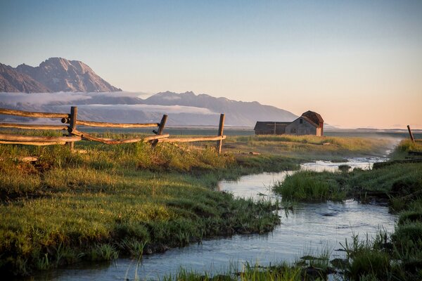 A lonely house on the bank of a stream. Sunset, mountains