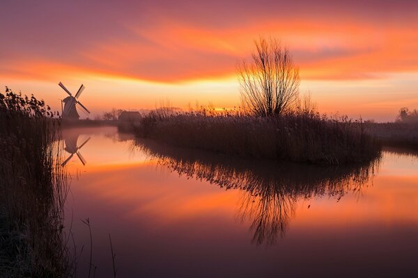 Sunrise on the background of a lake and a mill