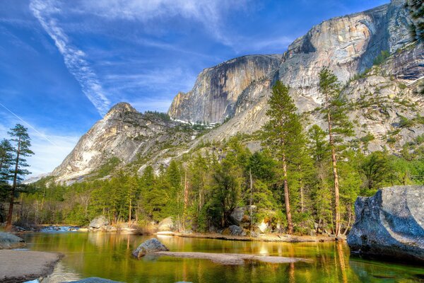 Mighty rocks stand behind the forest. The river overflowed below