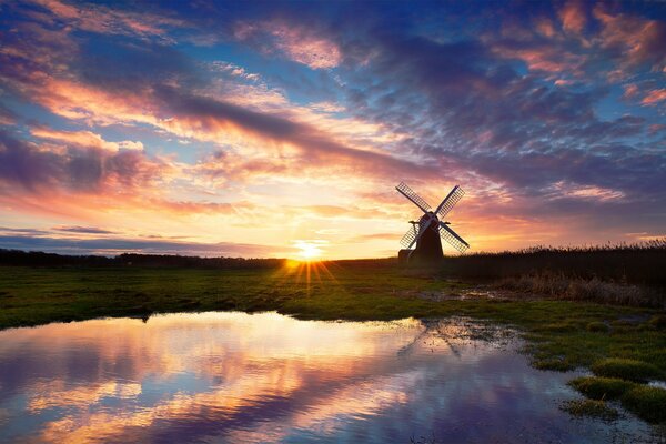 The mill stands on the birch of the lake. A beautiful sunset is reflected in the water