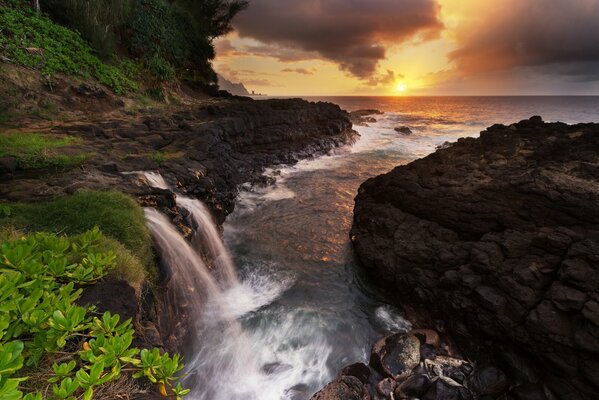 Wasserfall vor dem Hintergrund des Meeres und der Felsen bei Sonnenuntergang