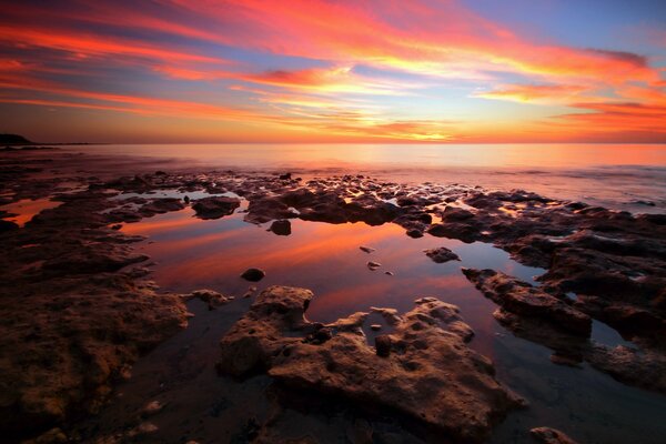 Stone beach. The dawn is reflected in the sea. Beautiful landscape