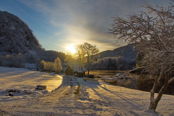 Sonnenuntergang und Berge. Verschneite Straße zum Haus am Fluss