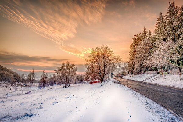 Paisaje de invierno con camino nevado y puesta de sol