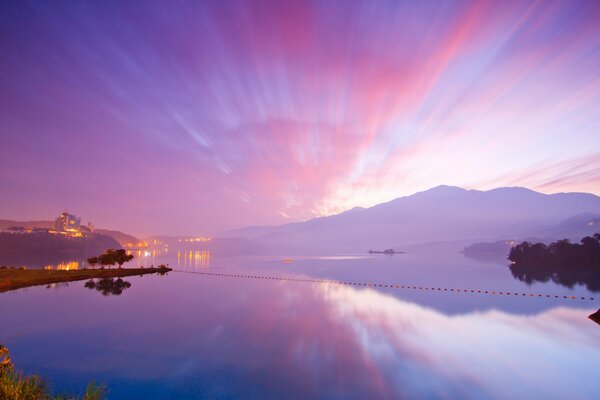 Bright pink clouds are reflected in the coastal waters against the background of mountains