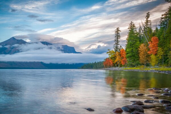 Le montagne tra le nuvole e la foresta si riflettono nel lago