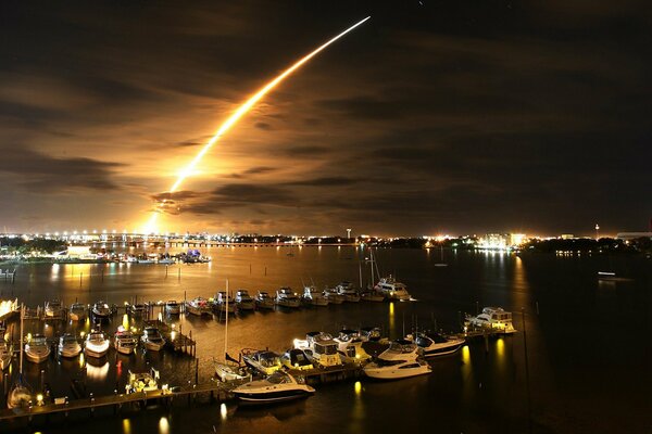 Trace de feu dans le ciel nocturne au-dessus de la jetée avec des yachts