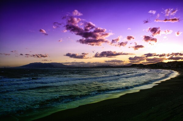 Сиреневый закат над пляжем, пускающем волны на берег