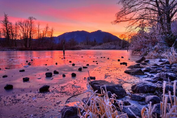 Winter, sunset in the mountains. Trees by the river with stones