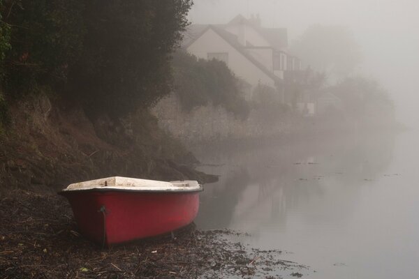 The bank of the foggy river with a red boat