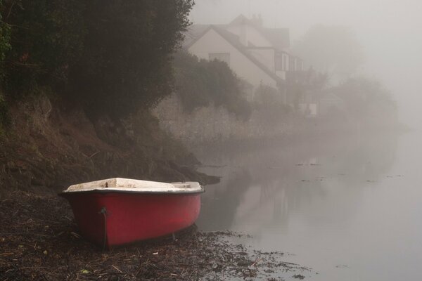 Brzeg mglistej rzeki z czerwoną łodzią