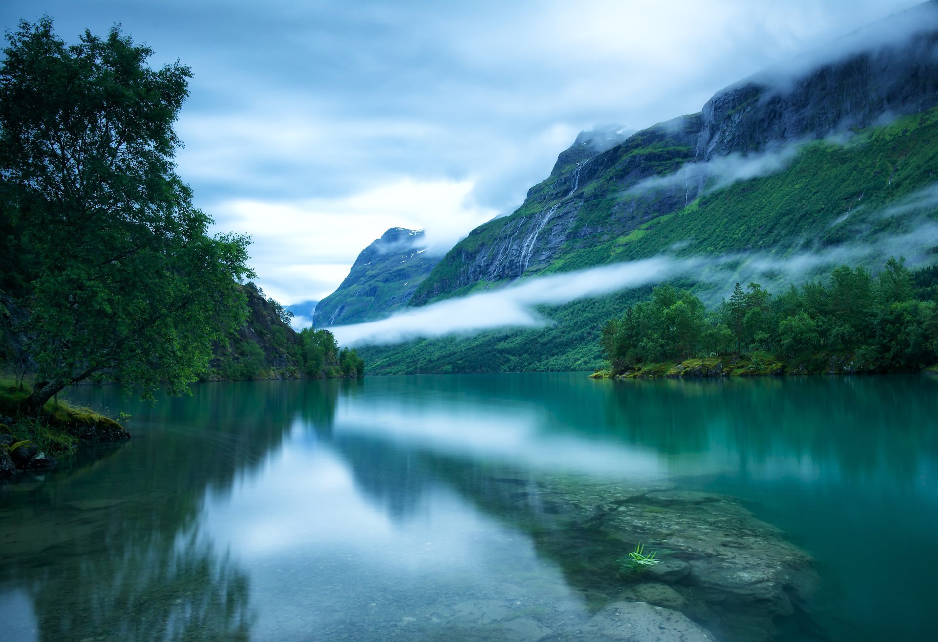 norvegia occidentale loenvatnet loen lago superficie liscia fondo pietre montagne scandinave alberi nebbia cielo nuvole