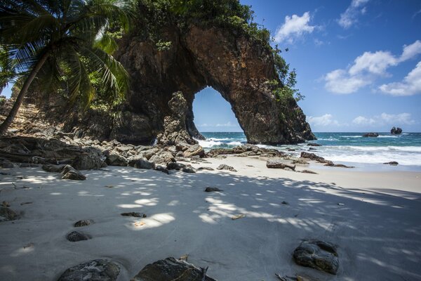 The rock behind the white beach. Palm trees and clouds