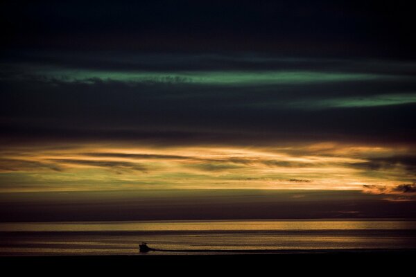 Im Meer haben sich die Wolken verdickt, aber das Boot ist bei Sonnenuntergang sichtbar