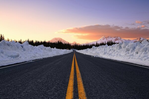 Straße mit gelben Markierungen und Schneewehen am Straßenrand