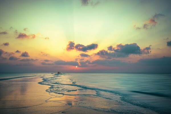 Schöner scharlachroter Sonnenuntergang vor dem Hintergrund eines spazierenden Paares am Strand