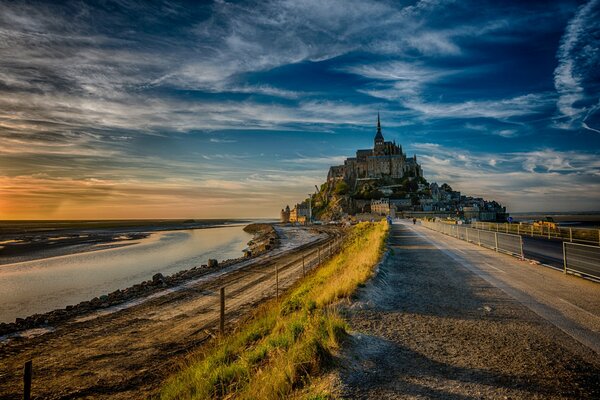 Château de l île du Mont-Saint-Michel dans les rayons du soleil du soir sous un ciel bleu avec des nuages