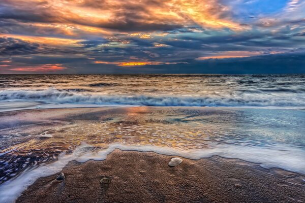 Sonnenuntergang in den Wolken am wunderschönen Sandstrand mit blauen Wellen